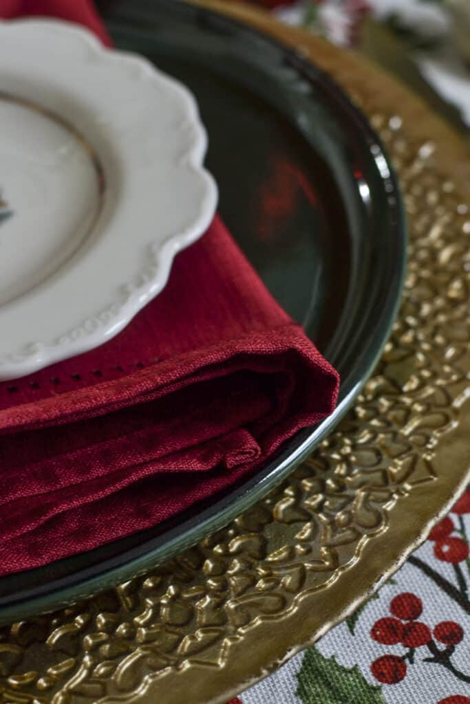 close up of a place setting on a Christmas table with gold charger, green dinner plate, red napkin and white appetizer plate.