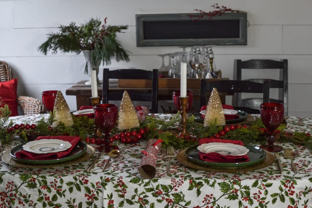A cozy cottage style Christmas tablescape with a boldly holly patterned tablecloth and red, green and gold place settings.
