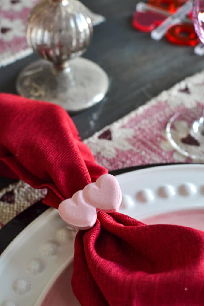 A red napkin with a pink candy ring pop used as a napkin ring.