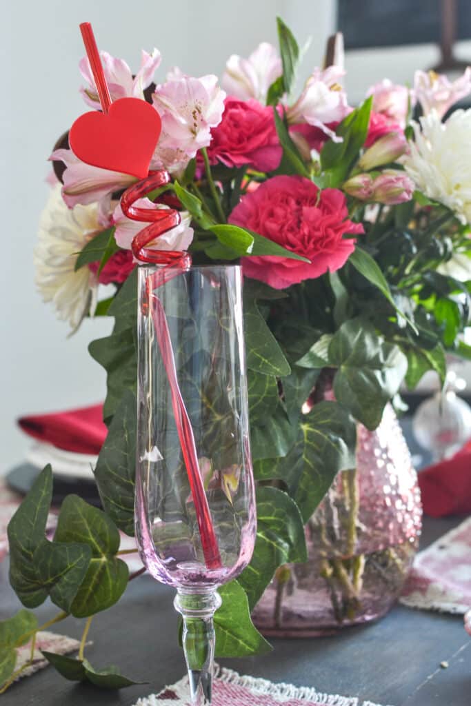 Whimsical family valentines day ideas like A red curly straw with a red heart placed in pink Champagne flutes on a Valentine's Day dinner table