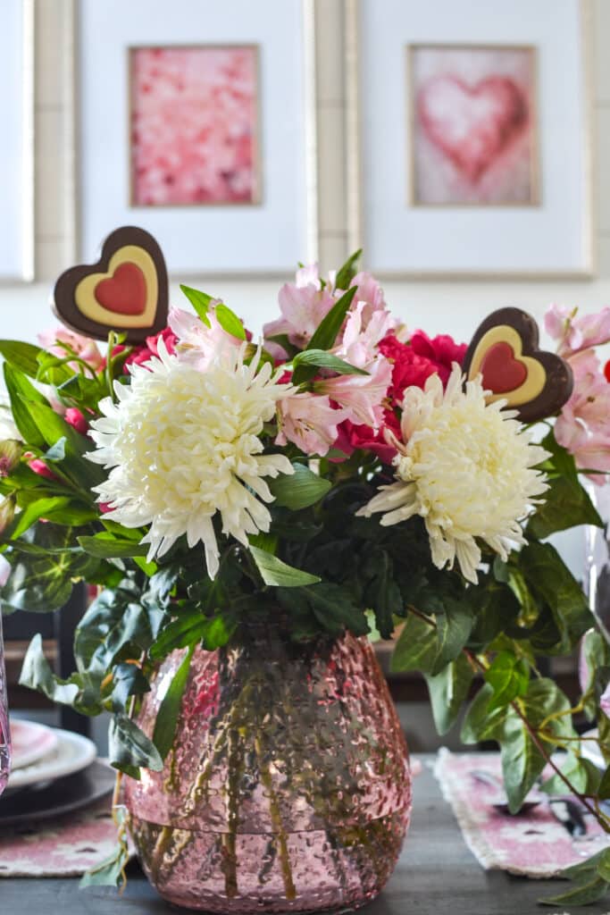 A Valentine's Day flower centrepiece with what mums, pink alsteromaria, and bright pink carnations, and chocolate hearts tucked in too.