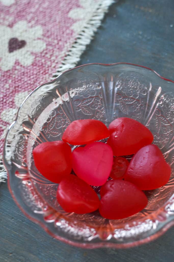 A pink depression glass dish filled with red and pink jujube heart candies.