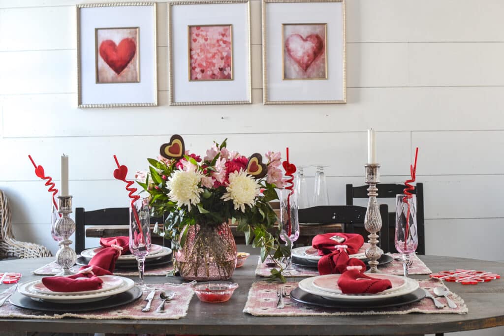 A Valentine's Day Table set with white plates, red napkins and a red and white floral centrepiece in a pink vase.