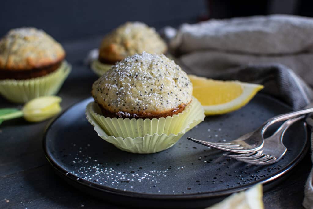 Lemon and poppy seed muffin sprinkled with confections sugar, served on a plate with antique forks.