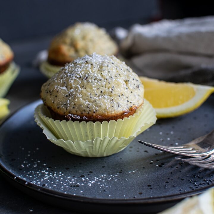 Lemon and poppy seed muffin sprinkled with confections sugar, served on a plate with antique forks.