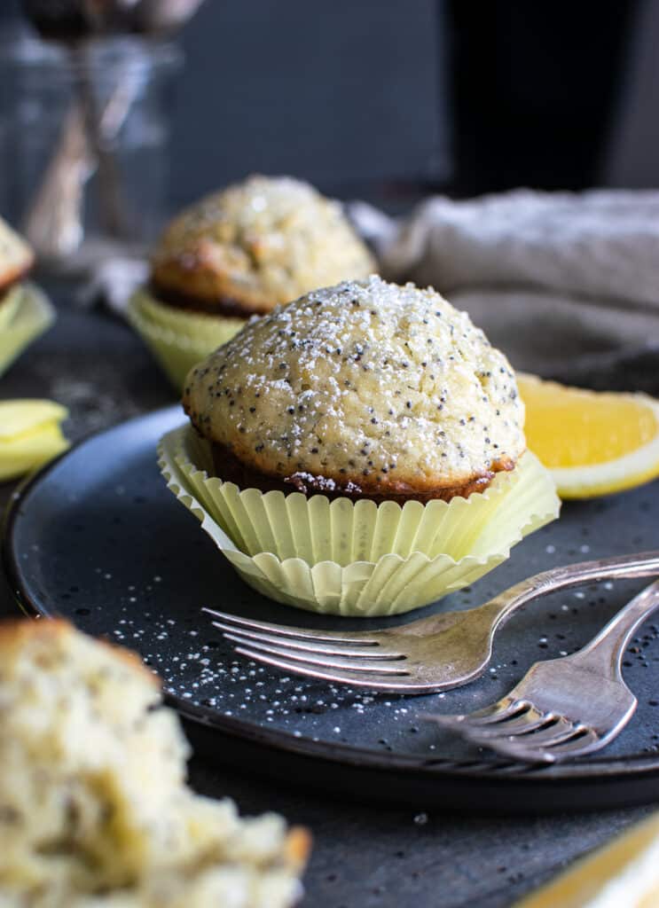 Lemon poppy seed muffin in a yellow cupcake liner, on a blue plate with 2 forks.
