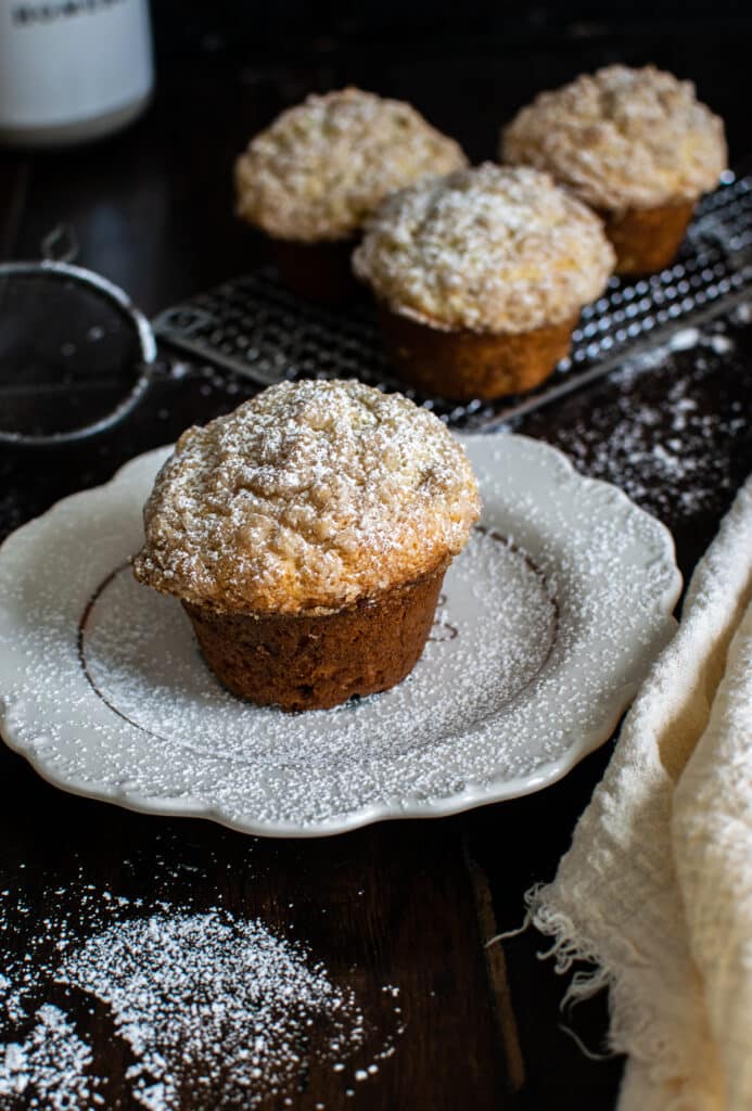 Banana Crunch Muffin made with greek yogurt is pictured on a white plate and sprinkled with confectioners sugar.