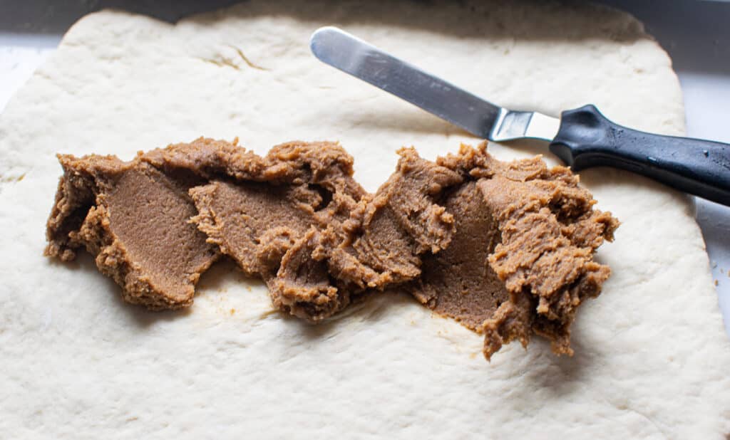 Dough for cinnamon rolls rolled out and cinnamon filling is being spread onto it.