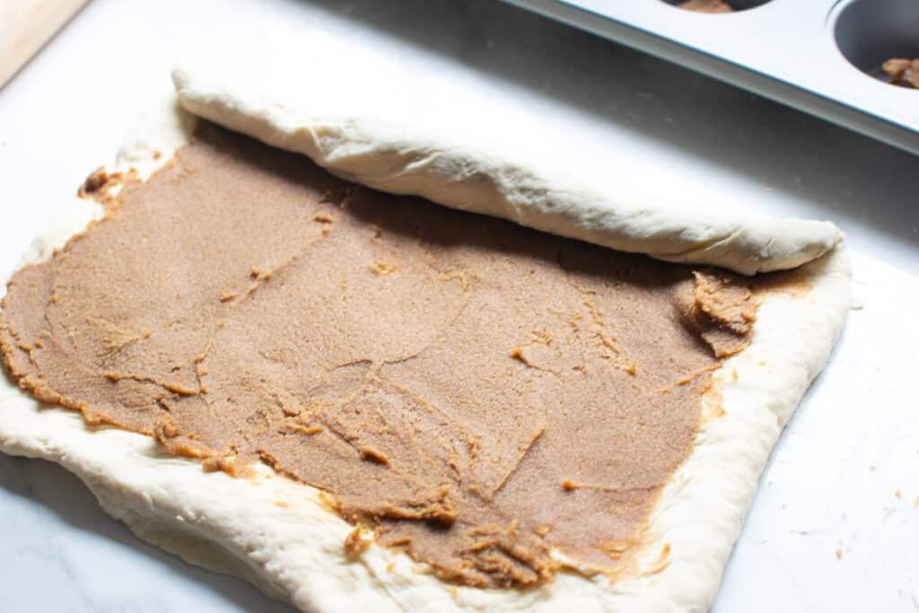 Rolling dough spread with cinnamon sugar mixture to make cinnamon rolls.