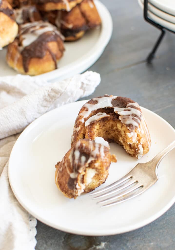 A cinnamon roll with a piece cut out and a fork on a white plate.