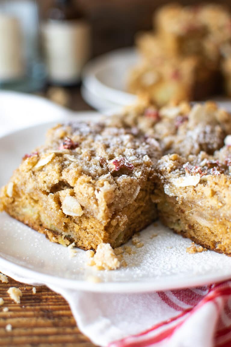 Rhubarb cake dusted with powdered sugar sitting on a white cake plate.