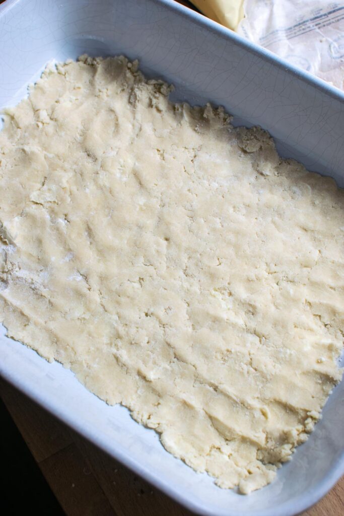 Shortbread dough pressed into the bottom of a glass baking dish.