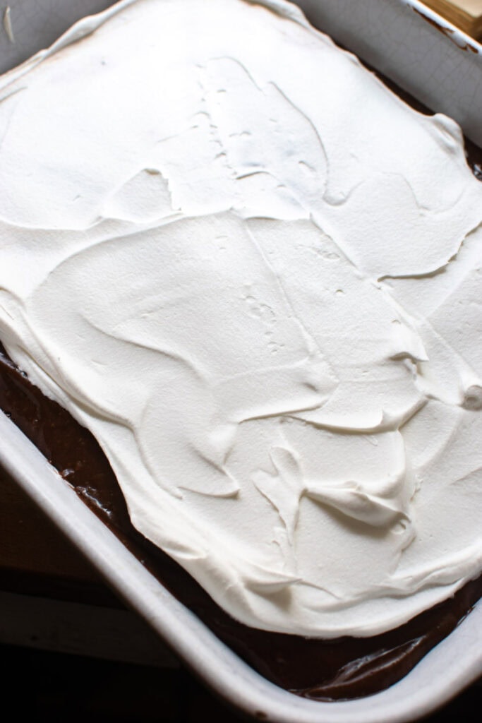 Whipped topping being spread over top of the chocolate pudding layer.