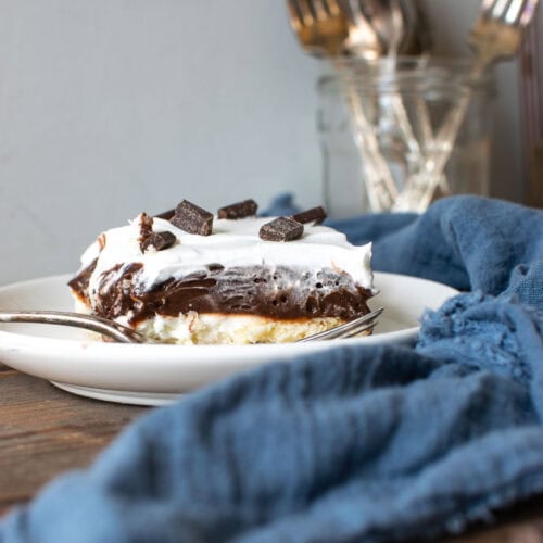 A slice of chocolate lush dessert on a white plate with a silver fork.