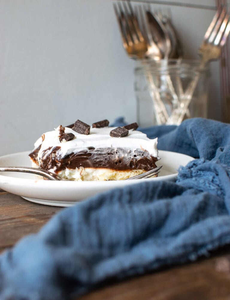 A slice of chocolate lush dessert on a white plate with a silver fork.