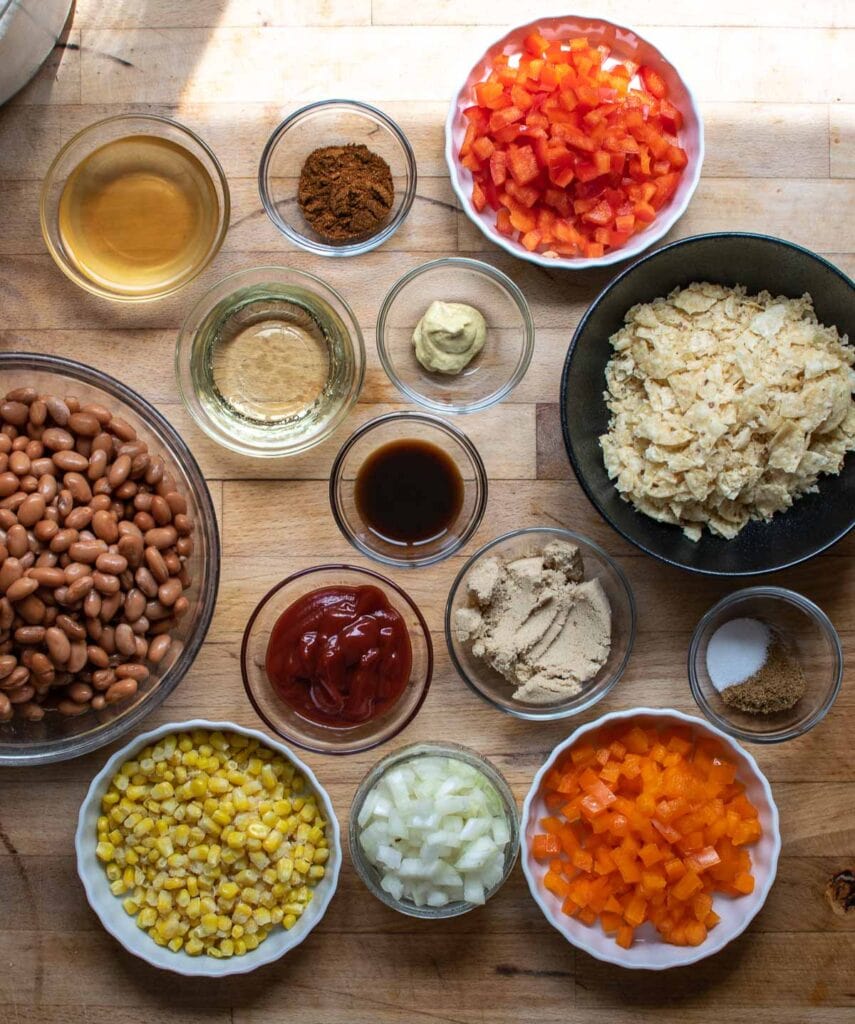 All the ingredients to make baked bean salad including pinto beans, spices, mustard, oil, vinegar, Worcestershire sauce bell peppers, onion and tortilla chips.