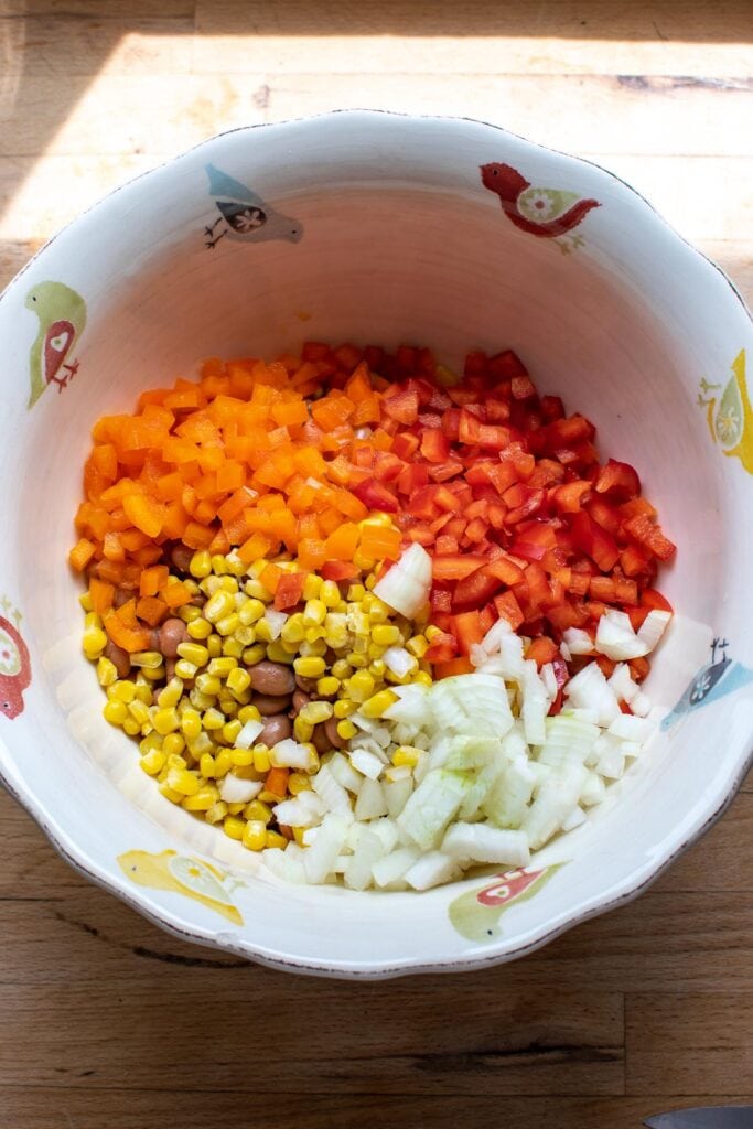Bell peppers, pinto beans, onion and corn in a large salad bowl before being combined.
