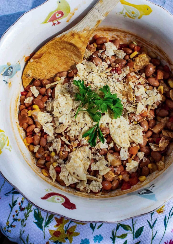 A large salad bowl filled with no-bake baked bean salad garnished with fresh parsley