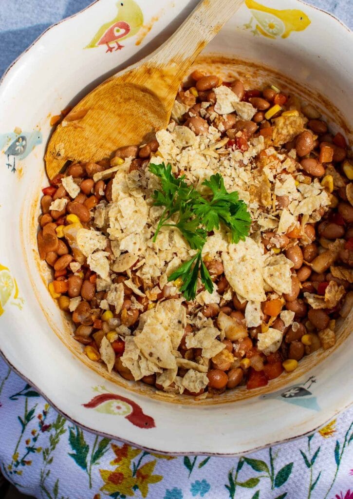 A serving bowl of baked bean salad topped with crushed tortilla chips and springs of parsley.