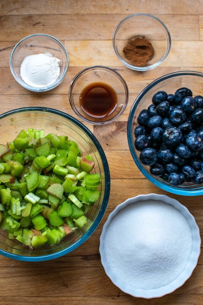 Ingredients to make filling for blueberry rhubarb crisp including fresh blueberries and rhubarb, sugar, and spices.