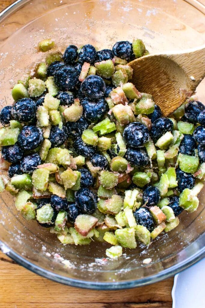 Ingredients for blueberry and rhubarb crisp mixed together in a glass mixing bowl.