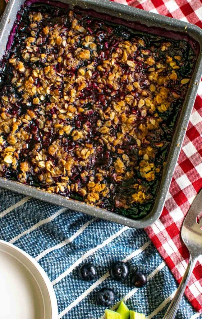 A pan of blueberry rhubarb crisp on top of a red and white checked napkin.