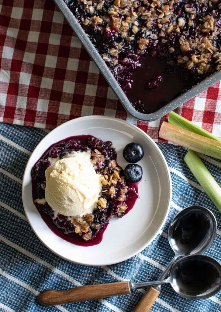 Overhead view of a blueberry rhubarb crisp with a scoop of ice cream on top.