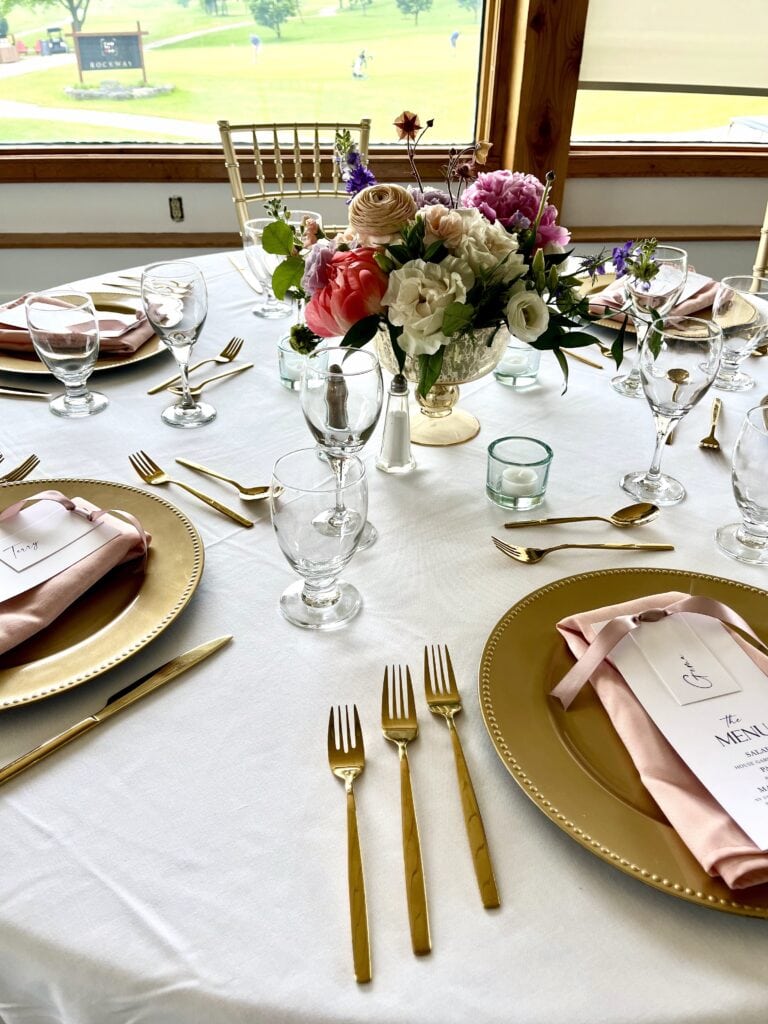 A wedding table set with gold charger plates, gold flatware and a floral centrepiece.