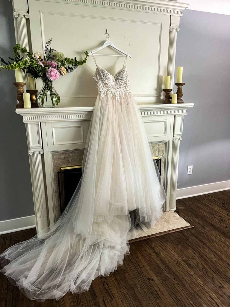 A wedding dress with narrow straps, a sweetheart neckline and full tulle skirt hanging in front of a fireplace.