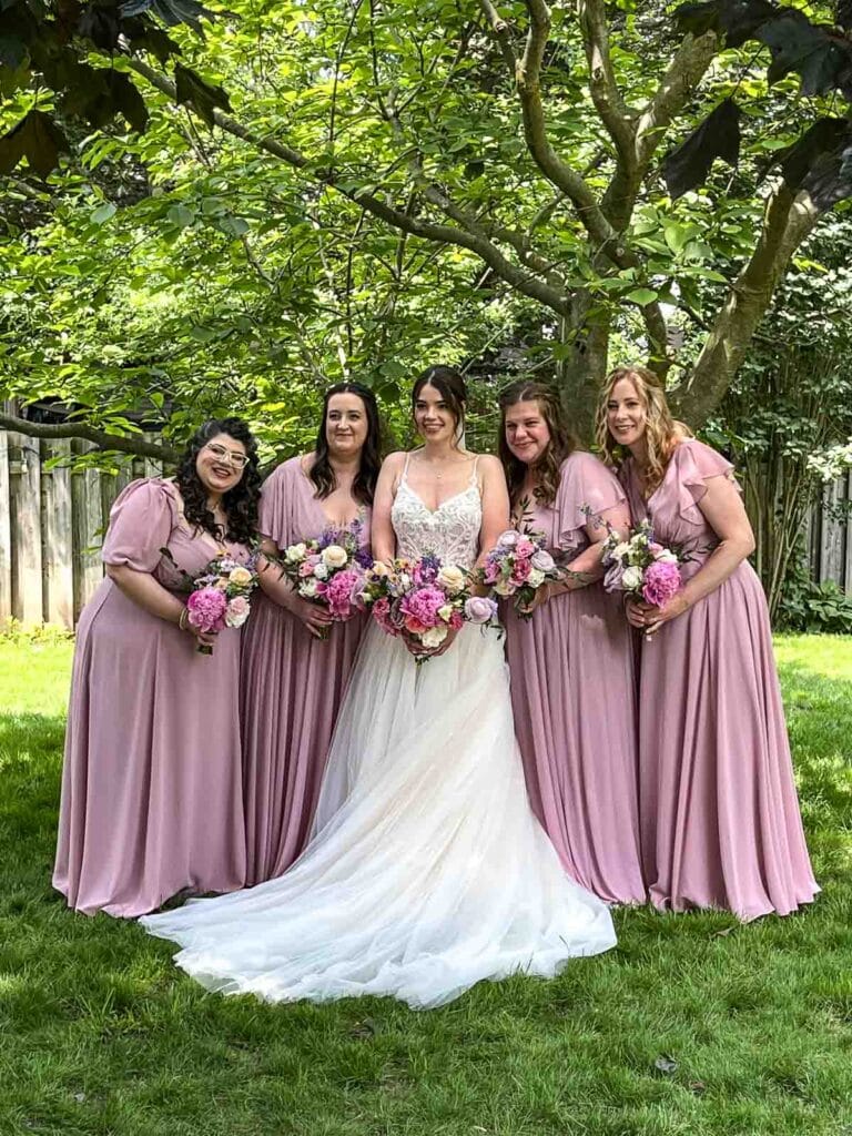 A bride and four bridesmaids who are wearing lavender long dresses.