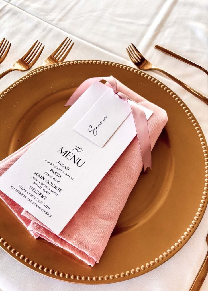 Wedding menu card tied with pink ribbon on top of a gold charger plate.