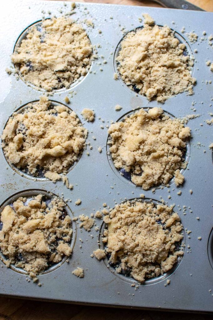 Crumble topping sprinkled over unbaked muffin batter in muffin tins.