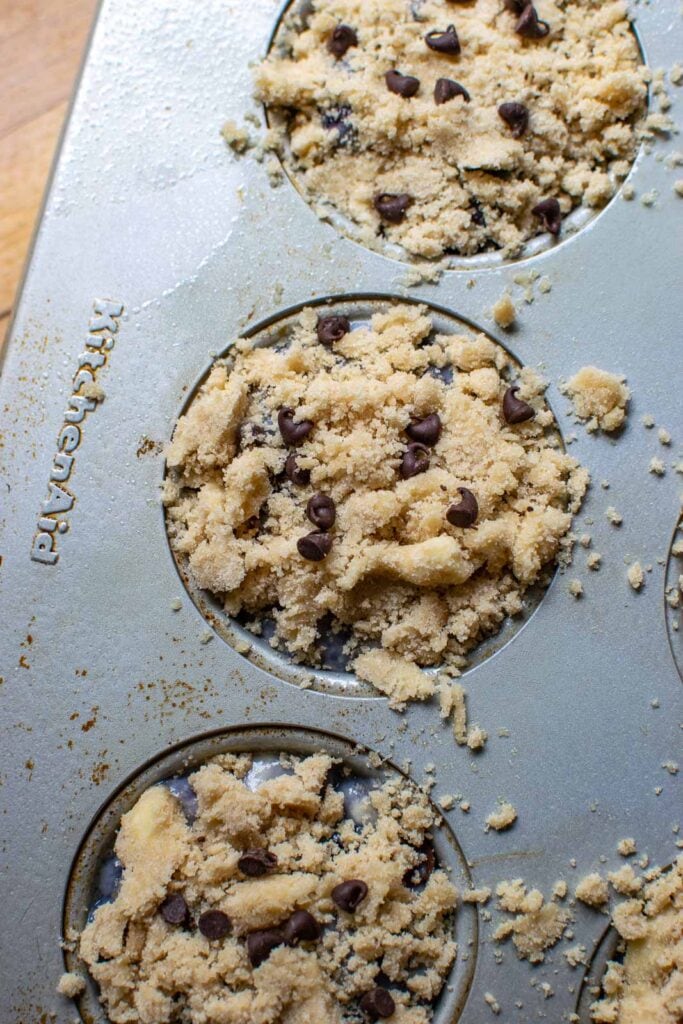 Mini chocolate chips sprinkled over top of the crumble topping on unbaked muffins.