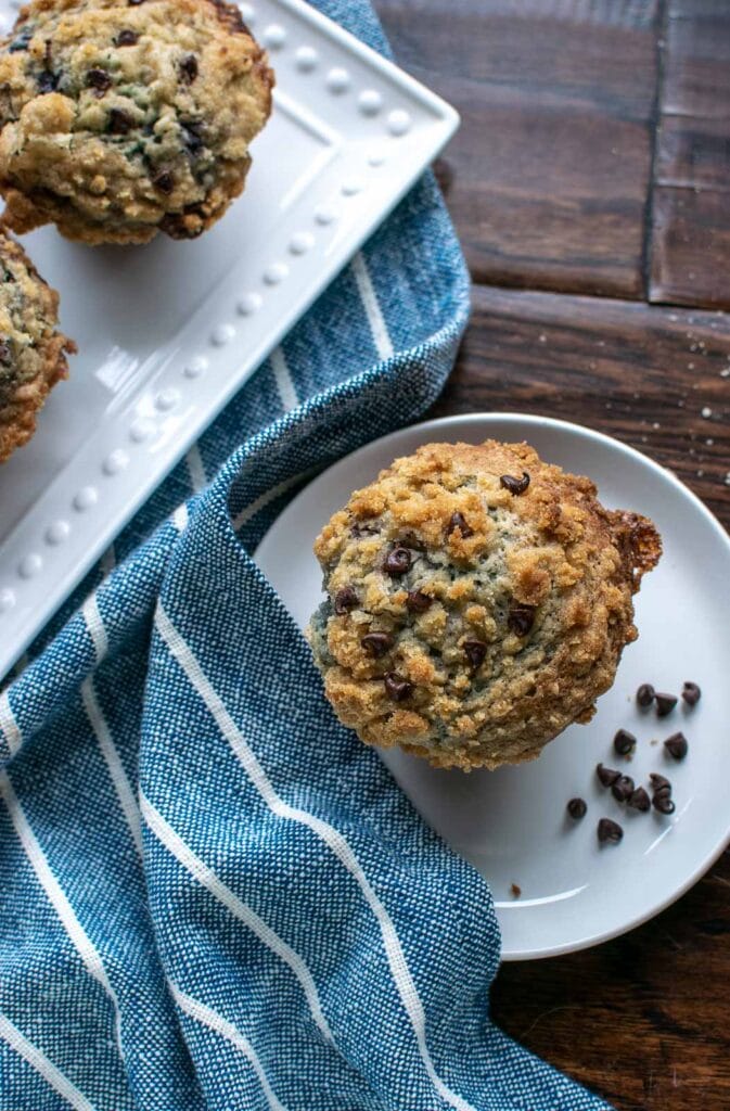 A blueberry chocolate chip muffin on a white plate with a blue and white striped napkin.
