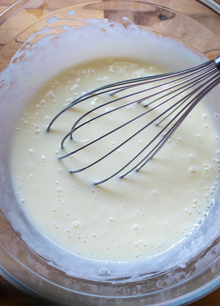 Thawed lemonade concentrate whisked together with sweetened condensed milk in a glass bowl.