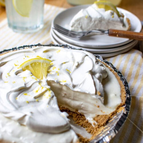 A lemonade pie with a slice cut out and placed on a white plate, with a glass of lemonade in the background.l