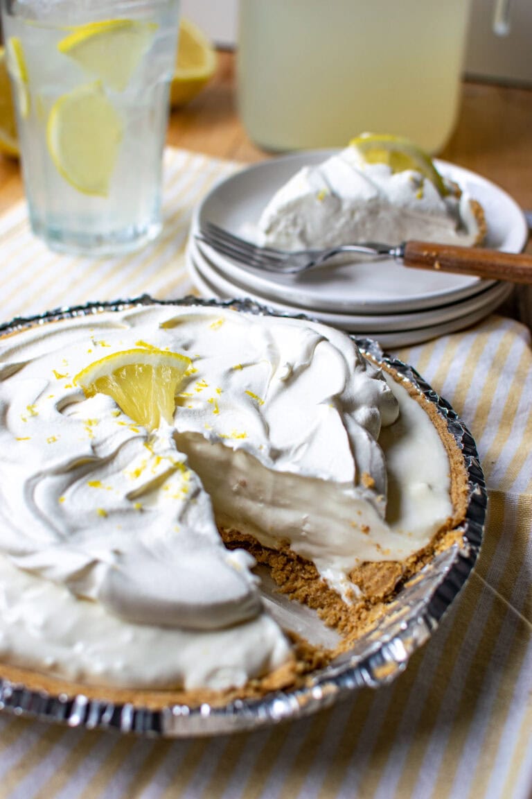 A lemonade pie with a slice cut out and placed on a white plate, with a glass of lemonade in the background.l