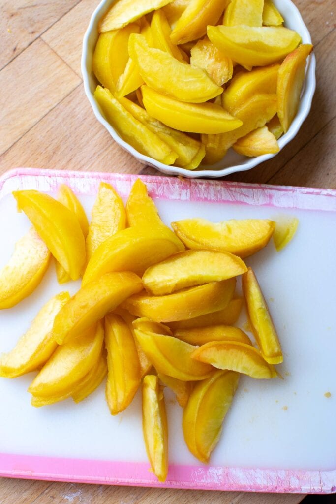 Peeled and sliced fresh peaches on a cutting board.