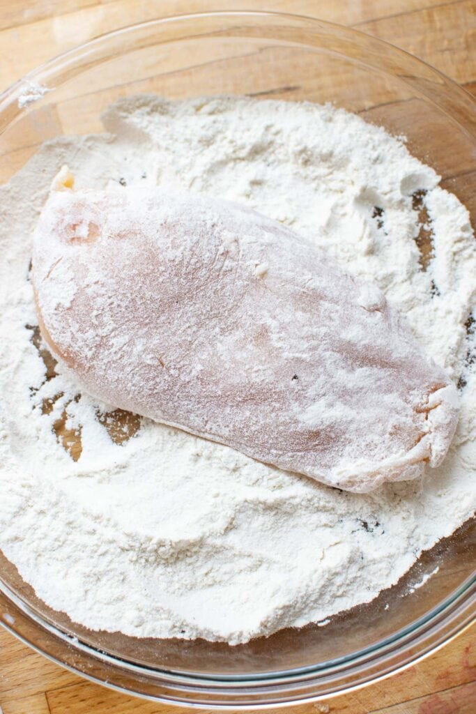 Fresh chicken breast being dredged in a flour, salt and pepper mixture.