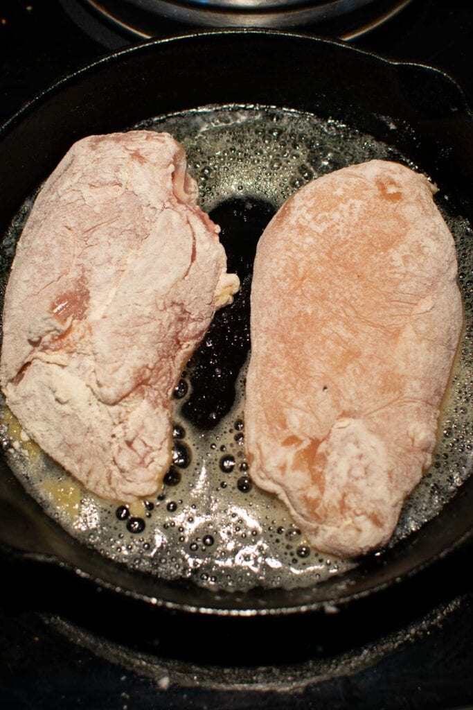 Chicken breasts that have been floured are being browned in a frying pan with butter.