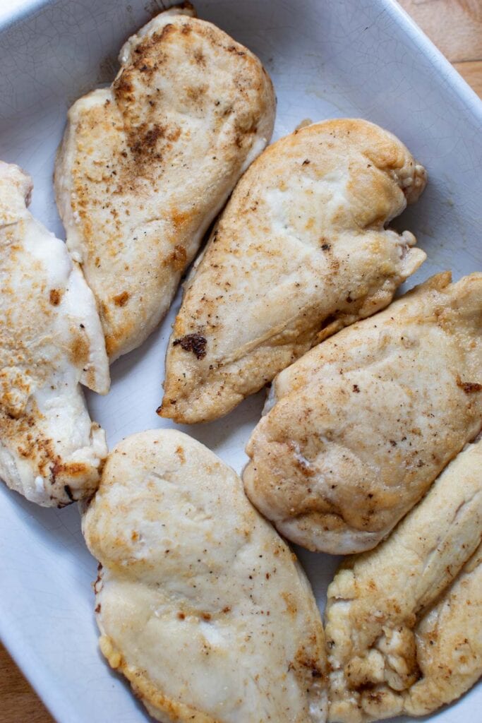 Boneless, skinless chicken breast that has been brown in butter and ready to be baked in the oven.