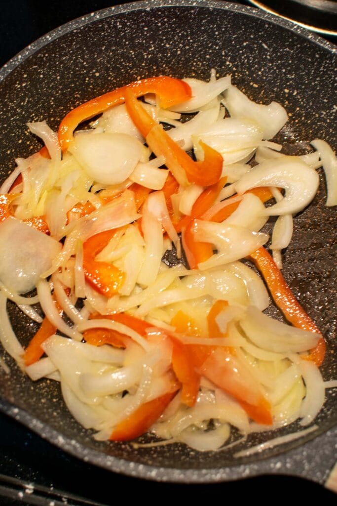Onion slices and pepper slices being fried in butter in a frying pan.
