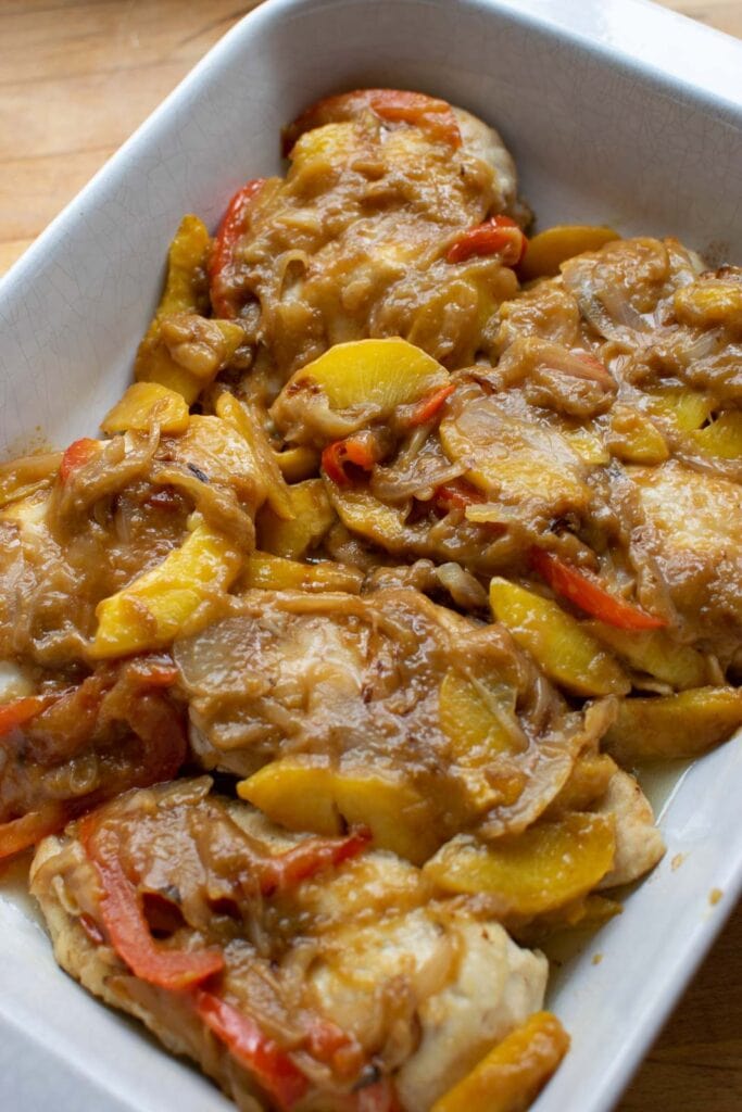 Baked chicken with a fresh peach sauce in a glass baking dish.