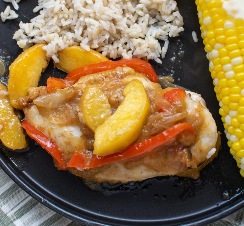 Baked peach chicken served with rice and corn on the cob.