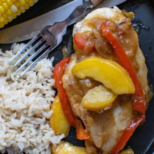 Chicken with peach sauce served with rice and corn on the cob.