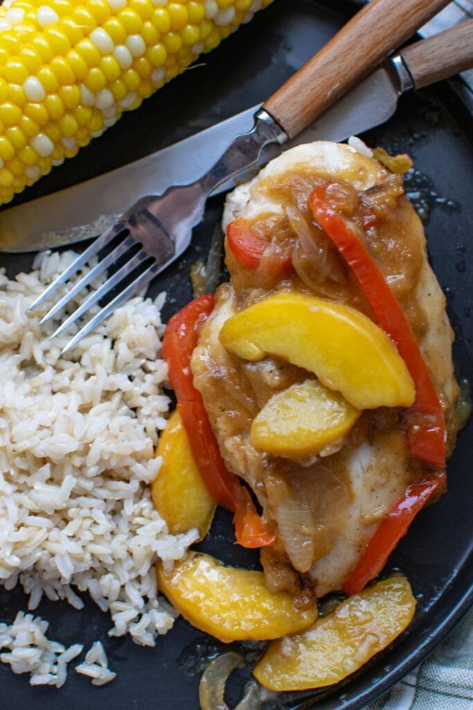Chicken with peach sauce served with rice and corn on the cob.