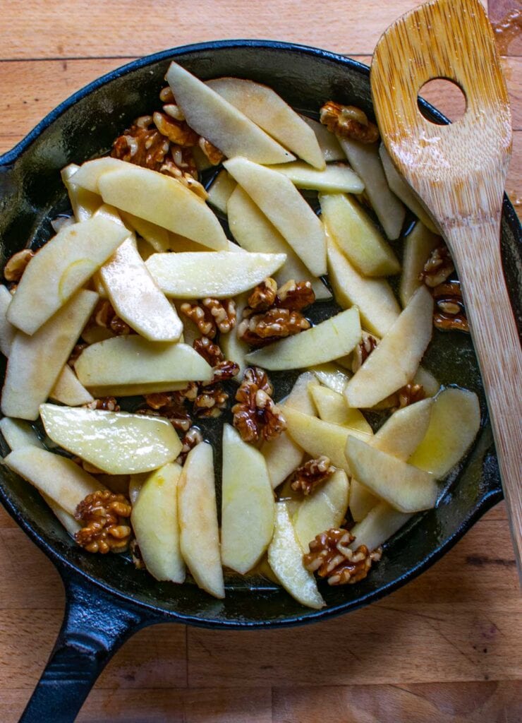 Apple slices and walnuts mixed with a maple syrup and butter sauce in a cast iron frying pan.