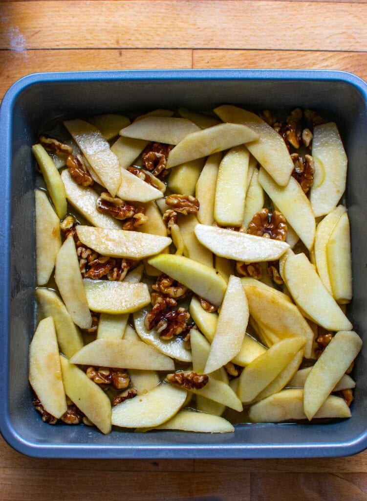 A mixture of apples, walnuts and maple syrup sauce in the bottom of a cake pan to make upside down cake.