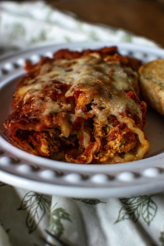 2 manicotti shells stuffed with cheesy chicken and spinach filling and covered in marinara sauce served on a white dinner plate.