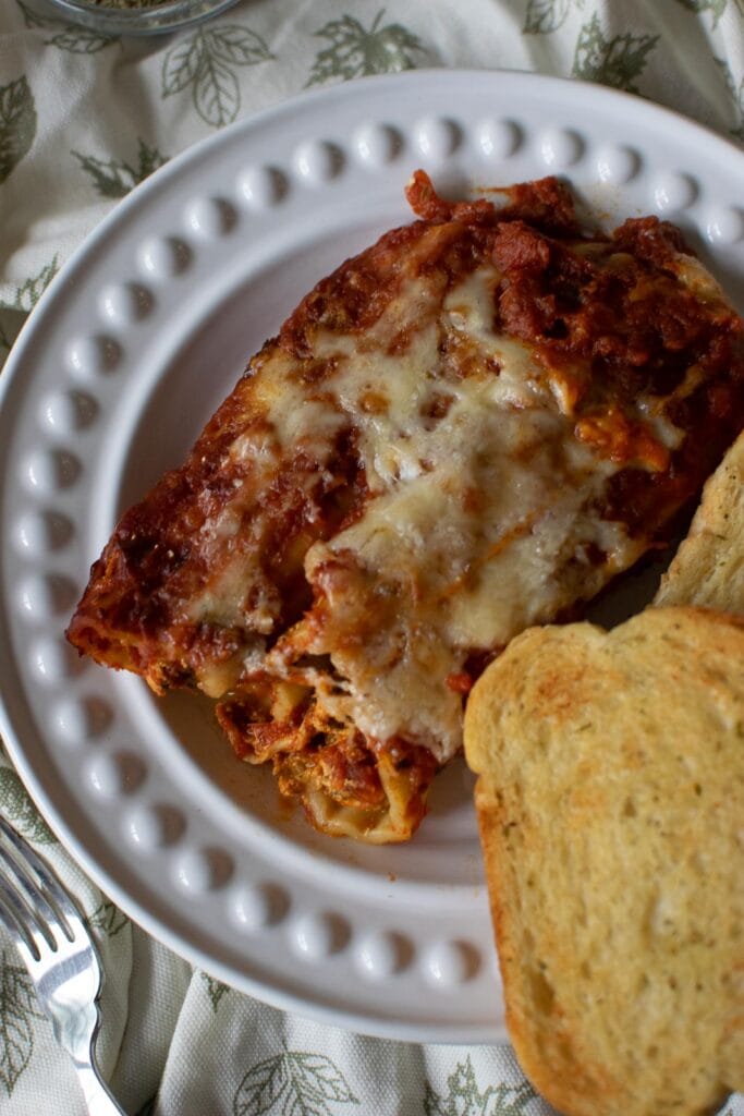 Chicken Spinach Manicotti on a white dinner plate and a side of garlic bread.